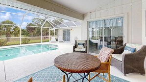 Ein überdachter Außenbereich mit Pool, Korbmöbeln und einer Glastür, die auf eine Terrasse führt.