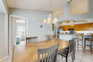 A dining area with a wooden table and chairs, a kitchen in the background, and a ceiling light fixture. - Spacious home with outdoor space & private pool (Rotonda West)