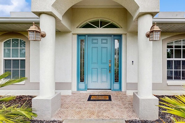 A building with a blue door, white columns, and two lantern-style lights. - Spacious home with outdoor space & private pool (Rotonda West)