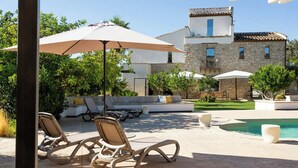 Une terrasse extérieure avec des chaises longues, une piscine et un bâtiment en pierre en arrière-plan.