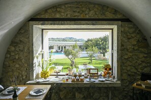 A stone-framed window with a view of a pool and greenery. - 18th century farmhouse in Racalmuto countryside (Racalmuto)