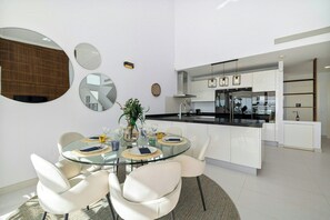 A modern kitchen with white cabinets and a glass island, a dining area with a glass table and white chairs, and a large mirror on the wall.
