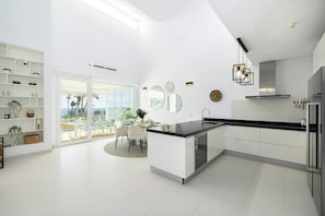 A modern kitchen with a central island, white cabinetry, and a dining area with a glass door leading to an outdoor patio.