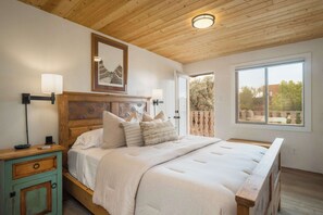 Ein Schlafzimmer mit Holzboden, einem Bett mit Kopfteil, Nachttischlampen, einem Nachttisch und einem Fenster mit Blick.