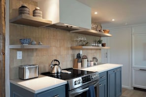 Eine moderne Küche mit eingebautem Herd, einem Toaster und Holzregalen über der Arbeitsfläche.