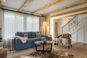 Ein Wohnzimmer mit blauem Sofa, rundem Couchtisch, Fellteppich, Holzboden und einer Treppe mit weißer Geländer.