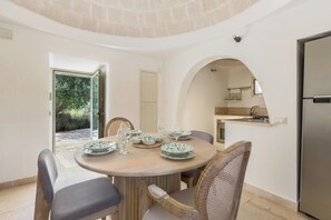 A dining area with a round table, chairs, and a view of the kitchen through an archway. - Trullo with private pool among olives in Ostuni (Ostuni)