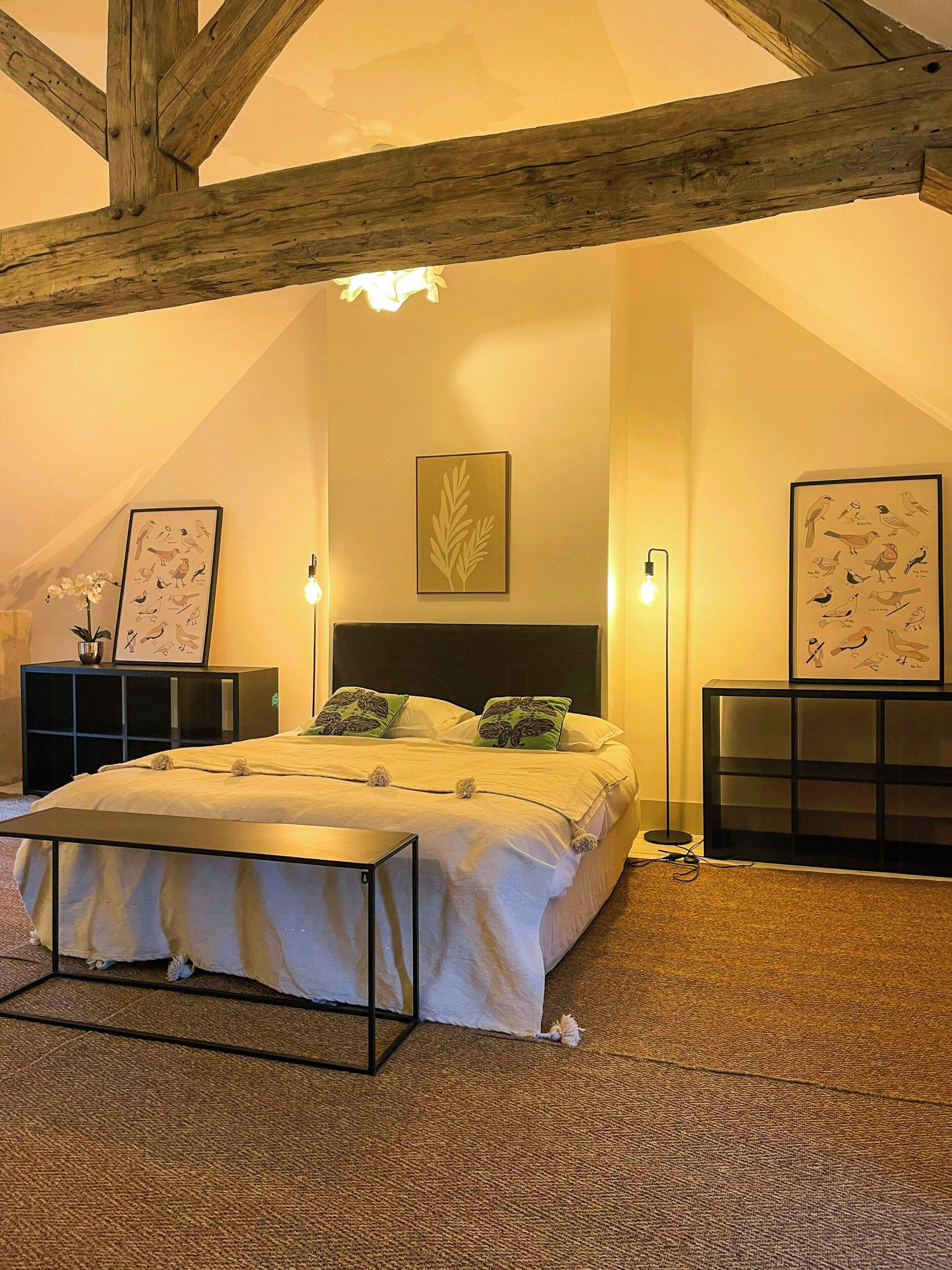 Ein Schlafzimmer mit Bett, Nachttischen, einer Wandleuchte und gerahmten Kunstwerken.