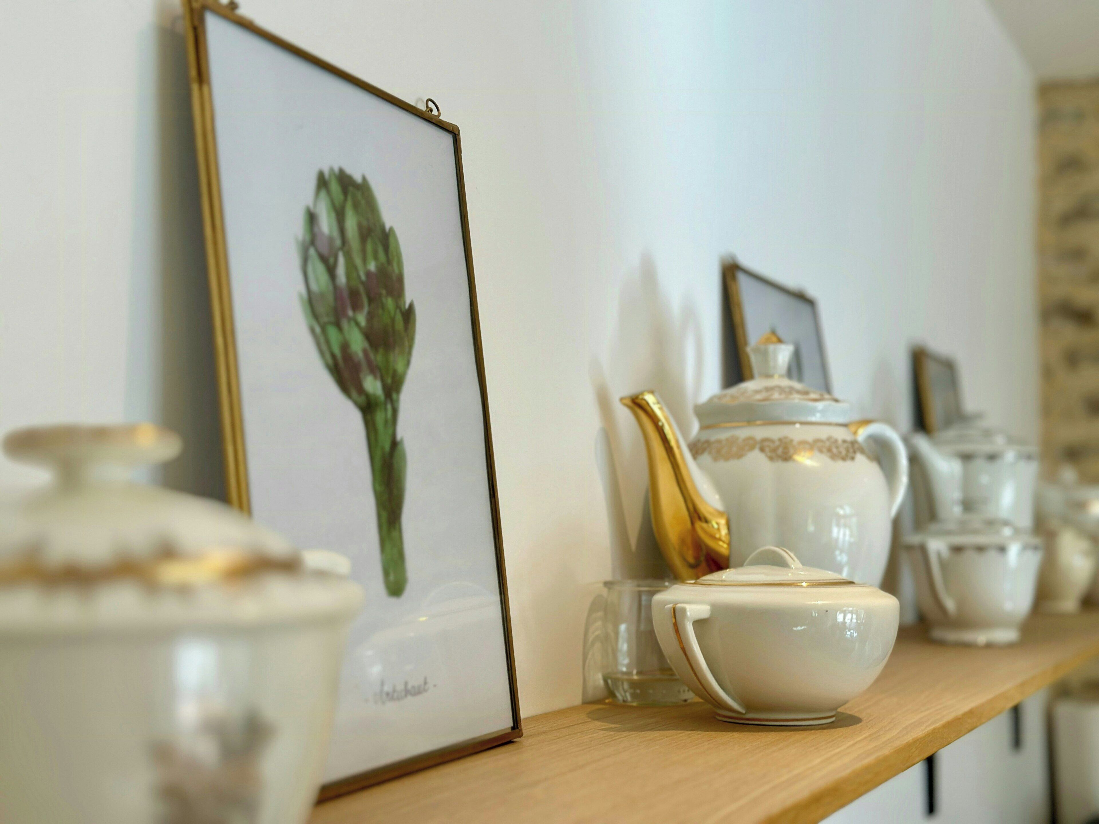 A shelf with white ceramic tea sets, a framed botanical illustration, and a gold-handled teapot.