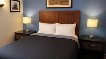 A neatly made bed with a dark-colored bedspread and two bedside tables with lamps, set against a blue wall with framed pictures above.