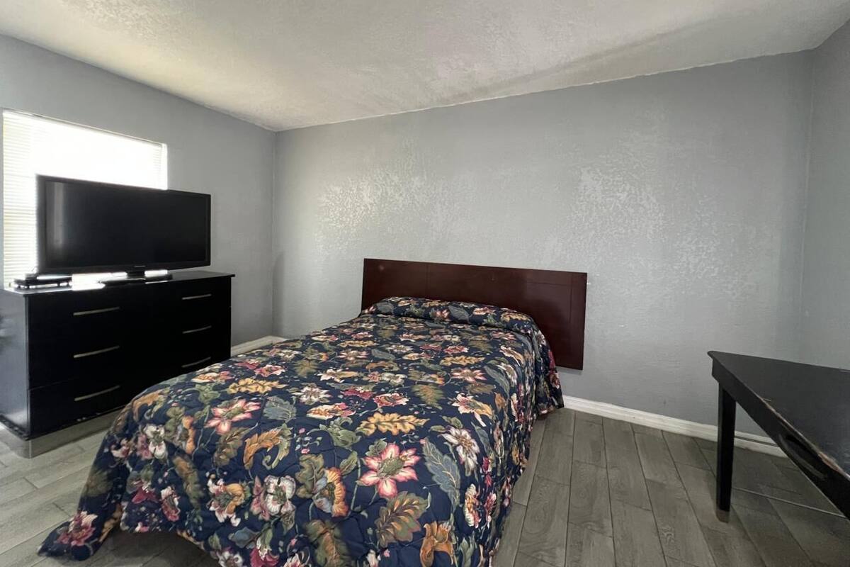Une chambre à coucher avec un lit, une commode, un téléviseur et un banc.