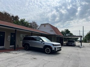 A building with a covered parking area, a gas station, and a vehicle parked in front.