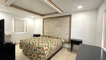 A bedroom with a bed, two bedside tables, a television, and a window with blinds.