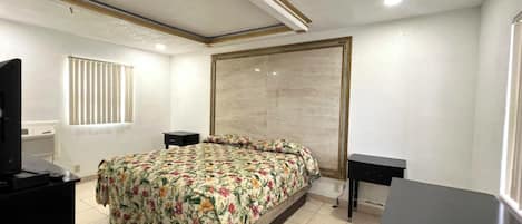 Een slaapkamer met een bed, twee nachtkastjes, een televisie en een raam met jaloezieën.