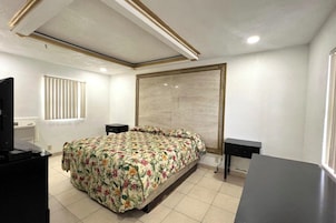 Un dormitorio con una cama, dos mesitas de noche, un televisor y una ventana con persianas.