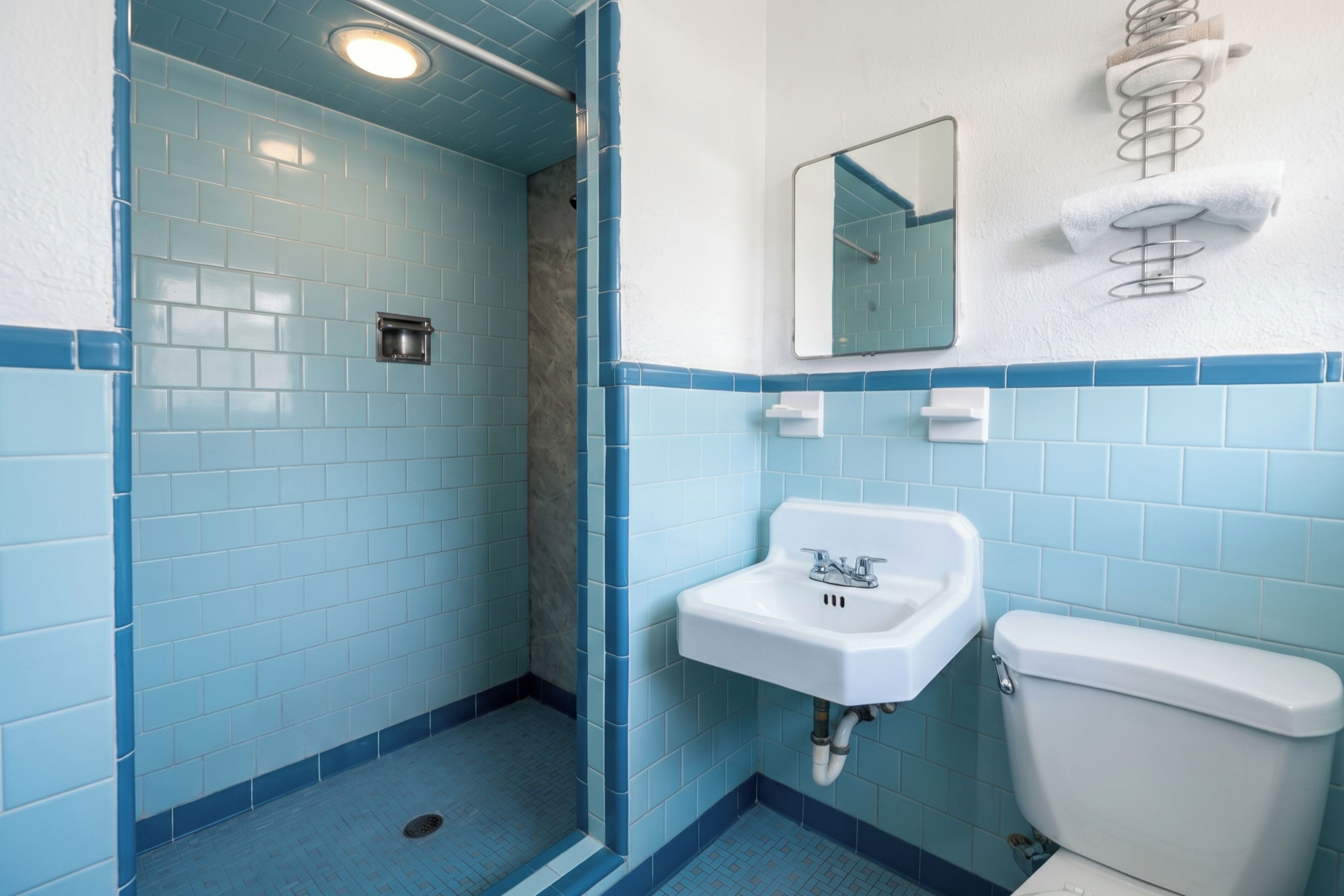 Un baño con azulejos azules, un lavamanos blanco y un inodoro.
