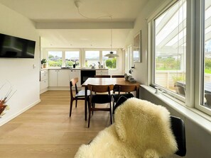 A modern kitchen with a dining area, large windows, and a flat-screen TV mounted on the wall. - Modern house at Sønderballe with private beach (Haderslev)