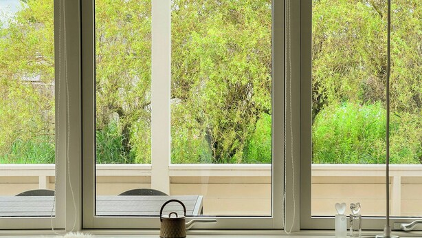 Ein Zimmer mit einem großen Fenster, einem gemütlichen Sessel, einem Wasserkocher und einer Lampe auf einem Tisch.