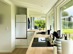 A modern kitchen with a built-in stove, a sink, and a window overlooking a garden. - Modern house at Sønderballe with private beach (Haderslev)