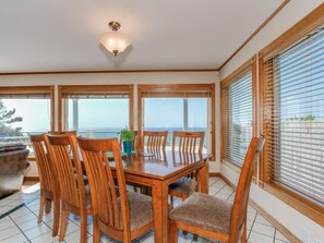 A dining area with a wooden table and chairs, large windows with blinds, and a ceiling light fixture. - Oceanfront Dreams~3 bedroom, 2200 square feet (Lincoln City)