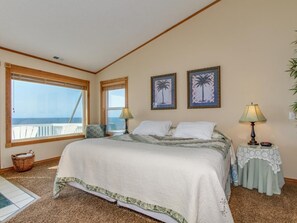 A bedroom with a large bed, two windows, a view of the ocean, and a small table with a lamp. - Oceanfront Dreams~3 bedroom, 2200 square feet (Lincoln City)