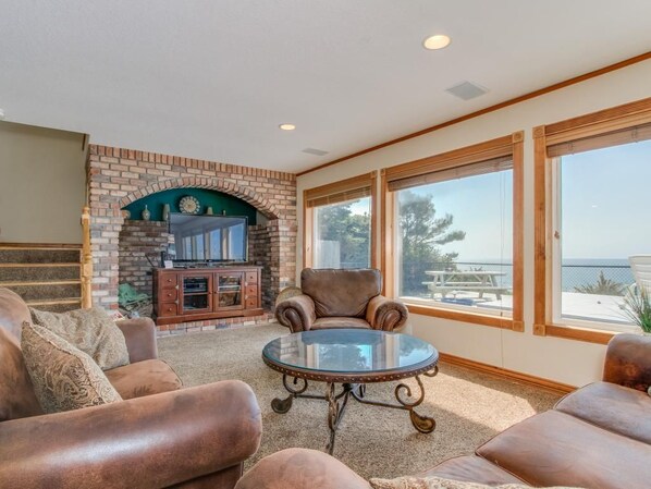 A living room with a brick fireplace, leather armchairs, a glass coffee table, and large windows with a view. - Oceanfront Dreams~3 bedroom, 2200 square feet (Lincoln City)