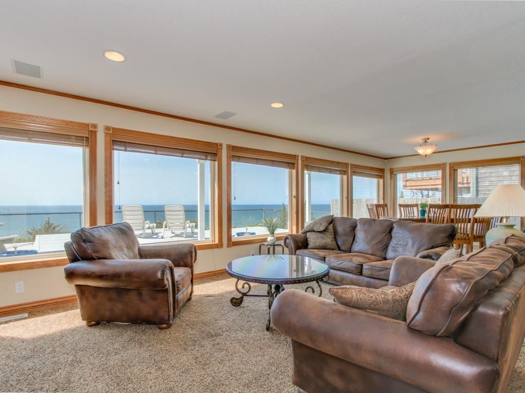 A spacious living room with leather sofas, a round coffee table, and large windows offering a view of the ocean.