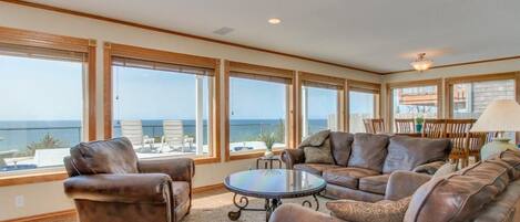 A spacious living room with leather sofas, a round coffee table, and large windows offering a view of the ocean.