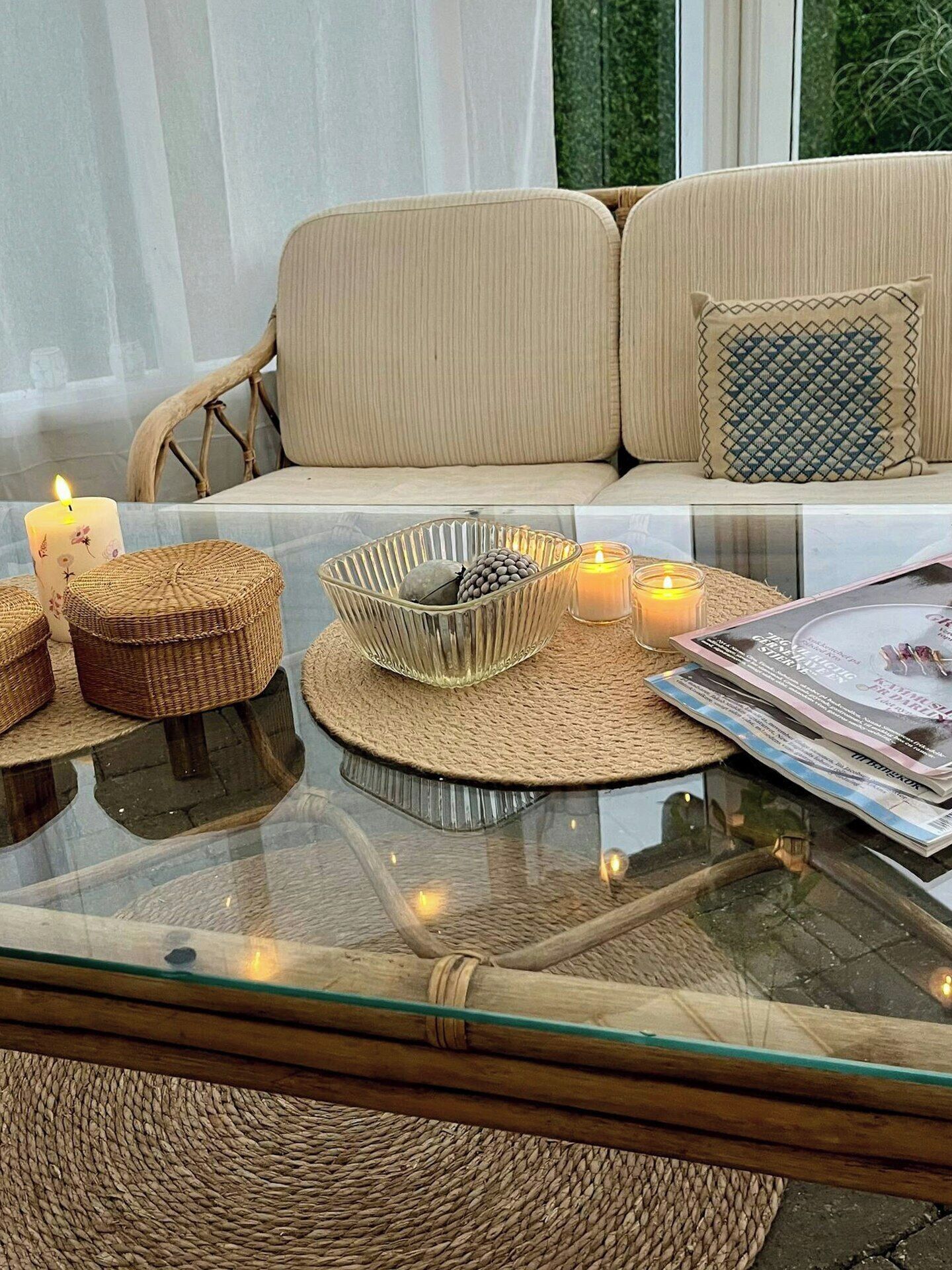 A glass-top coffee table with woven placemats, candles, and a magazine.