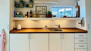 A kitchen with a wooden countertop, a sink, cabinets, a kettle, a teapot, and a window with a view. - Lovely summerhouse by the beach (Karrebæksminde)