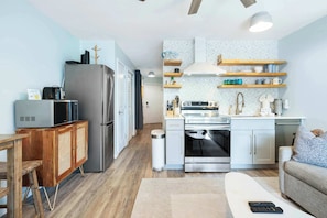 A compact kitchen with a refrigerator, microwave, stove, and wooden shelves.