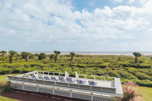 A deck with chairs overlooking a beach and manicured garden.