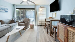 Ein Wohnzimmer mit einer Couch, Couchtisch, Fernseher, Deckenventilator und einem Essbereich mit Tisch und Stühlen.