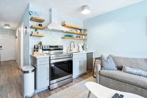 A modern kitchen with built-in appliances, wooden shelves, and a grey sofa.