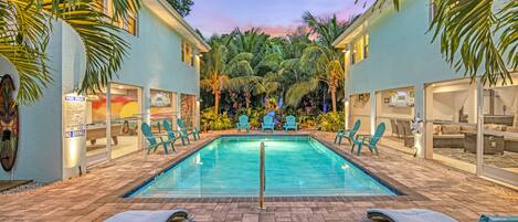 A swimming pool with lounge chairs, palm trees, and a sunset sky.