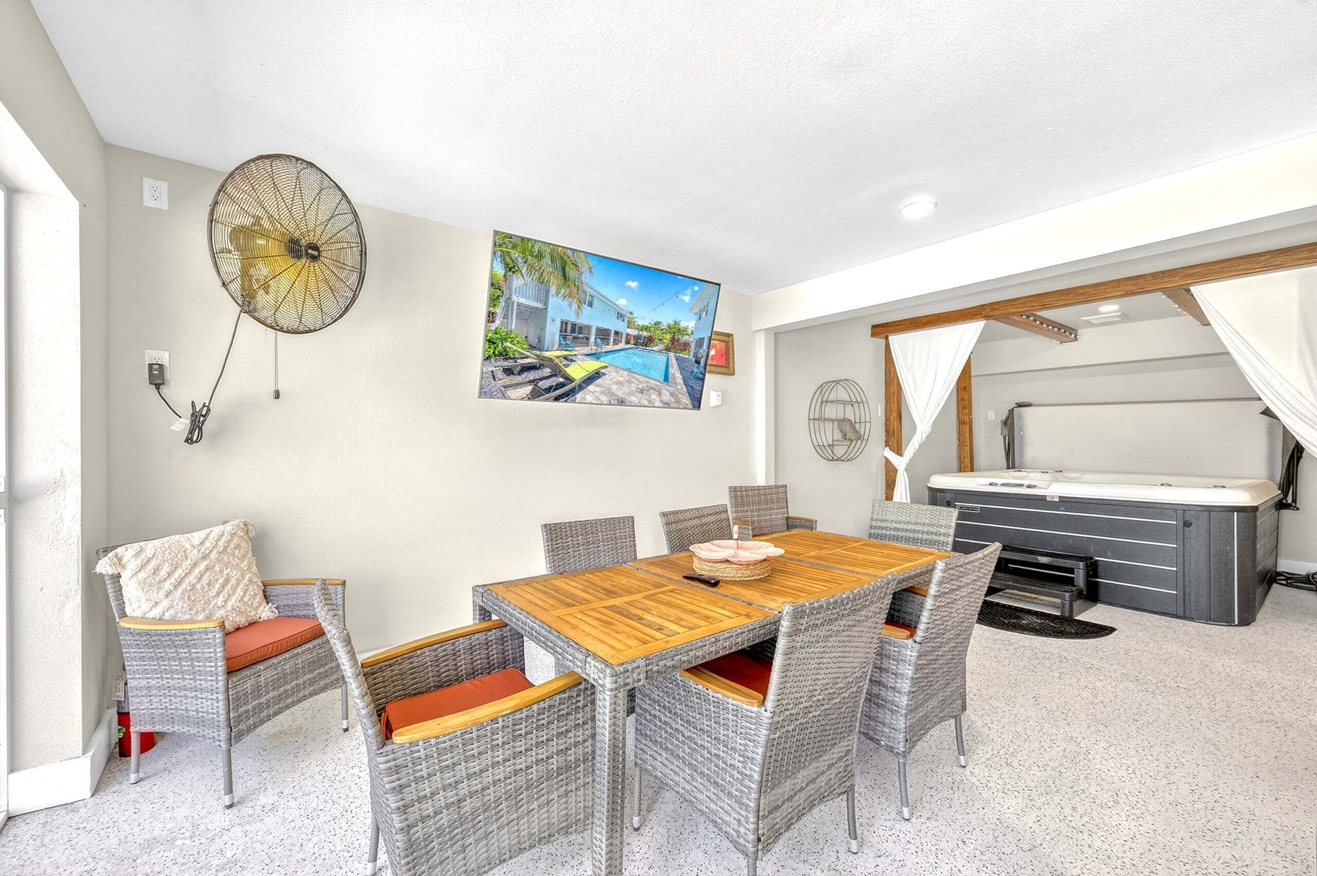 Ein Essbereich mit Holztisch und Korbstühlen, einem Wandventilator und einem Gemälde eines Pools.