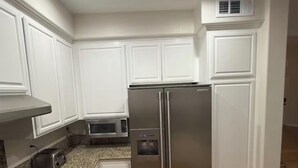 A kitchen with white cabinets, a stainless steel refrigerator, a microwave, a toaster, and a gas stove.