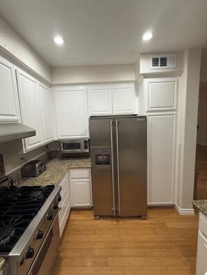 A kitchen with white cabinets, a stainless steel refrigerator, a microwave, a toaster, and a gas stove.