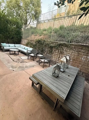 An outdoor patio with a wooden table, a light-colored sofa, and two chairs.