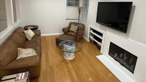 A living room with a brown sofa, a glass coffee table, a television, and a fireplace.