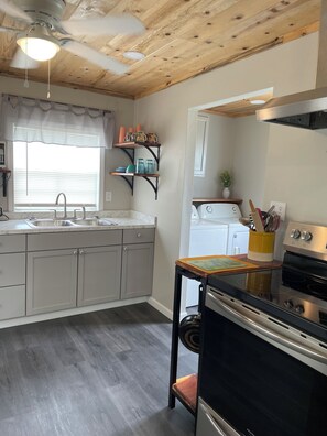 A kitchen with a wooden ceiling, a built-in oven, a sink, and a window with blinds.