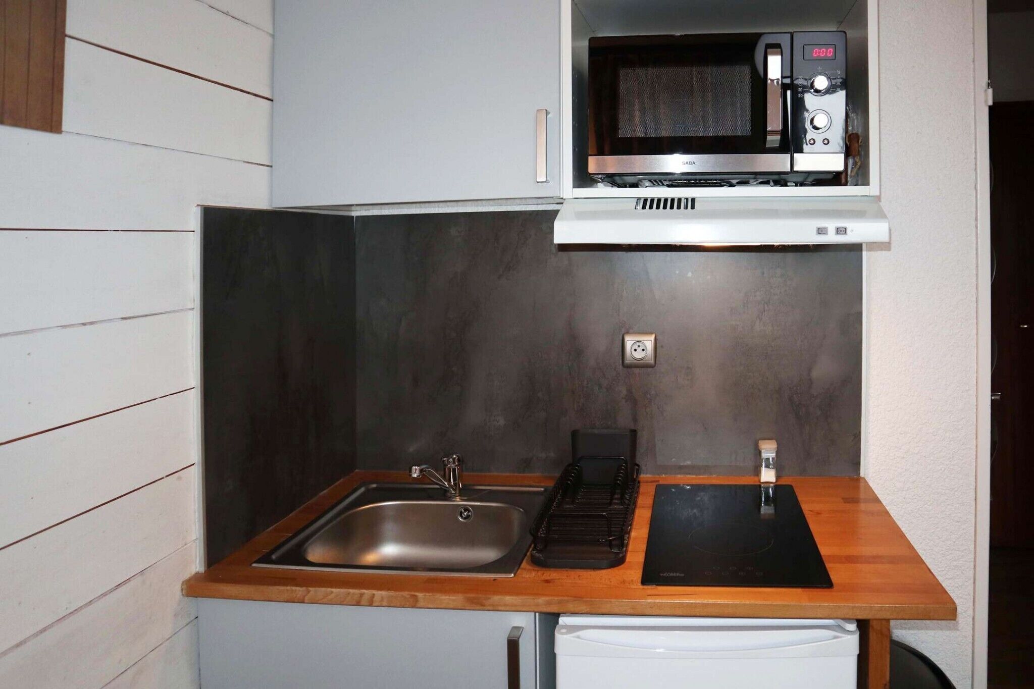 Een compacte keuken met een roestvrijstalen spoelbak, een zwart inductiekookplaat en een magnetron boven het aanrecht.