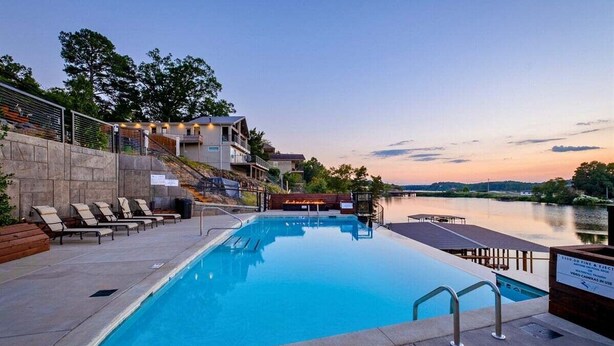 Une piscine avec des chaises longues, une terrasse en bois et une vue sur un lac au crépuscule.