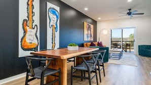 Un espace repas comprenant une table et des chaises en bois, un canapé et des œuvres d’art accrochées aux murs.