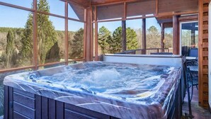 Ein Whirlpool in einer Holzhütte mit großen Fenstern und Blick auf Bäume.