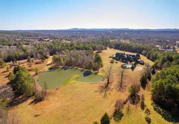 An aerial view of a property with a pond, a house, and surrounding forested area.