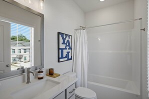 Un baño con lavamanos blanco, inodoro, ducha y ventana con persianas.