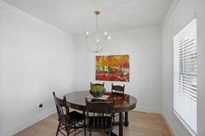 Comedor con una mesa redonda, cuatro sillas, una araña y un cuadro en la pared.
