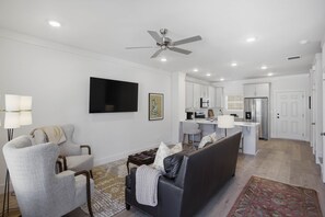 Una sala de estar moderna con un sofá, sillones, una mesa de centro, un televisor y un ventilador de techo.