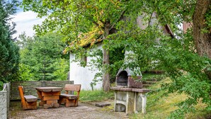 A rustic outdoor seating area with a stone table and benches, a brick-paved patio, and a stone fireplace. - Apartment 'Fichte' with Shared Terrace, Shared Garden and Wi-Fi (Sankt Georgen im Schwarzwald)